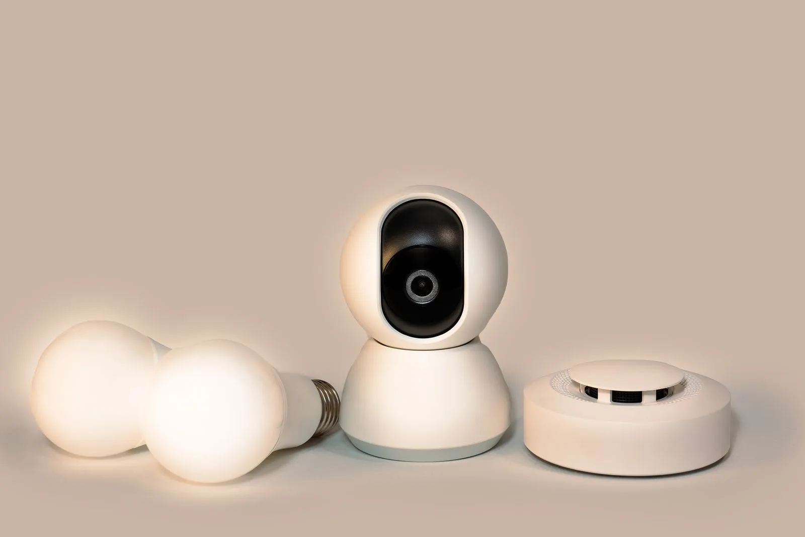 Smart security camera, two light bulbs and a smoke detector on a beige surface