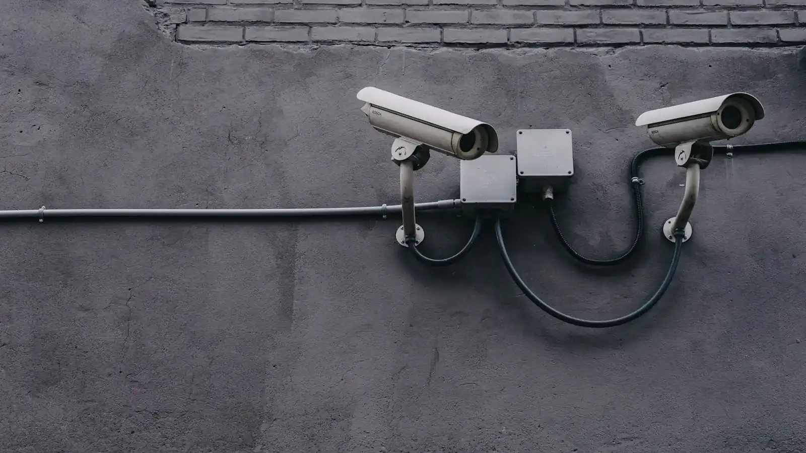 Two outdoor security cameras mounted on a dark wall